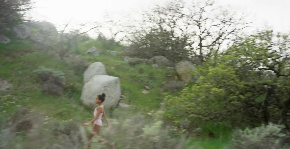 A young girl runs past trees on a hill
