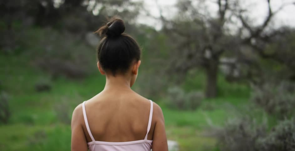 A girl walks up a hill passing trees and shrubs with pale leaves