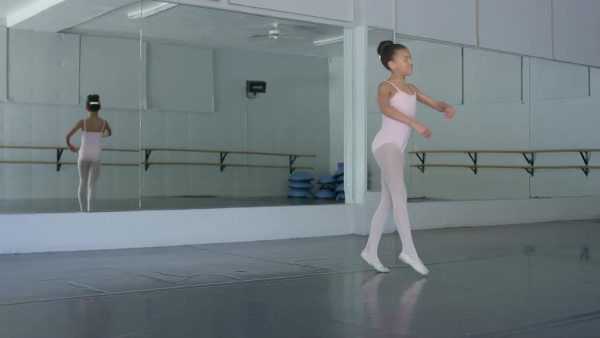 A young ballet dancer in a pink leotard and tights practices in an empty studio