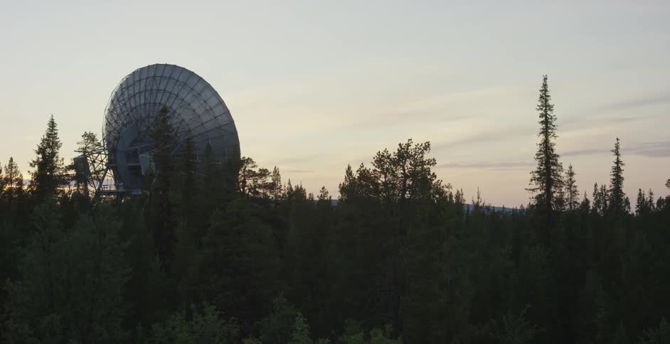 A large satellite dish pokes out above the tree line at dusk