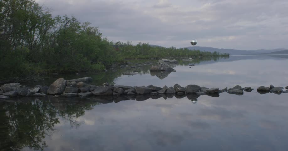 A silver ball floats over a pond on a cloudy day