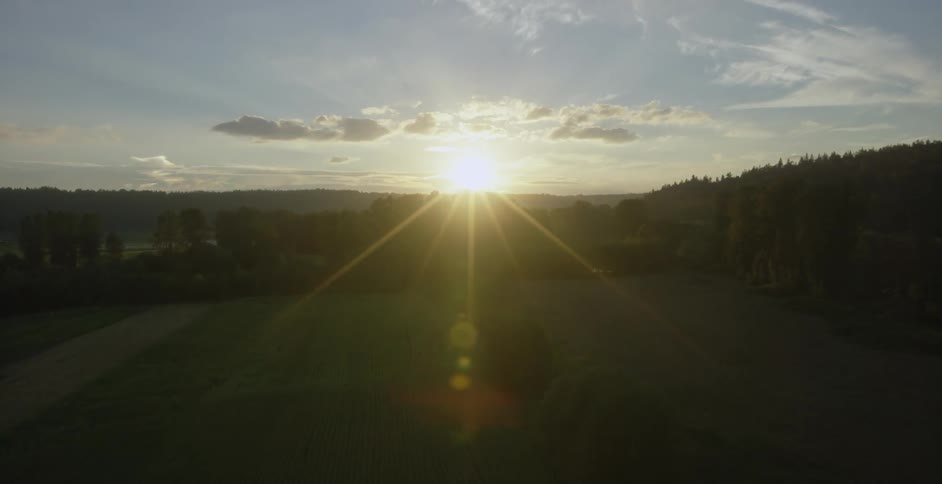 Slowly rising in the air above a field with the sun setting in the distance