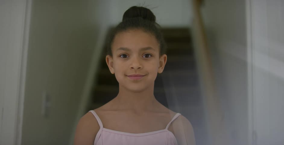 A little girl in a ballerina leotard standing and smiling