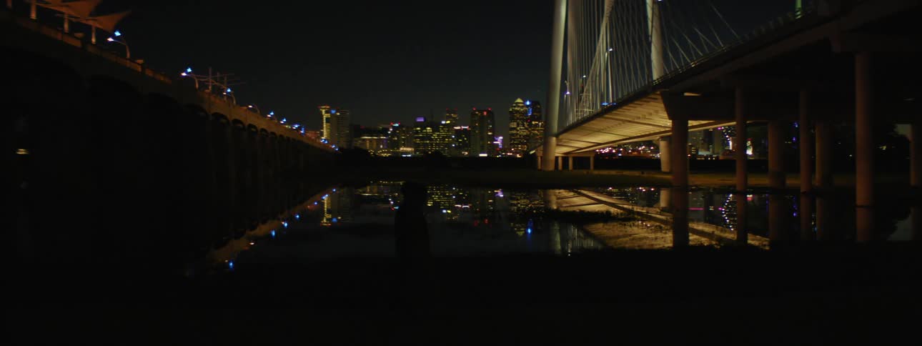 Two people walk in the dark towards a bridge