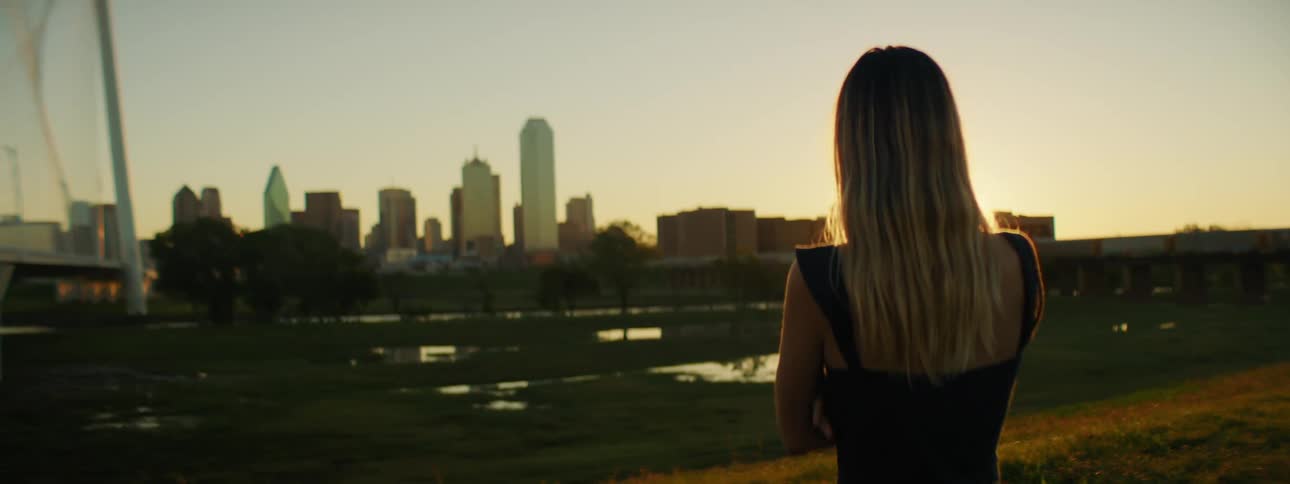 A woman is outdoors and looking at a city skyline
