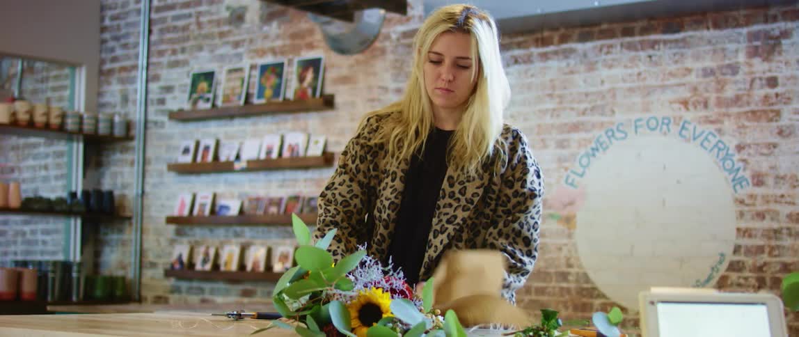 A florist wraps the stems of a flower arrangement with brown paper