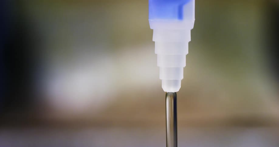 A plastic nozzle with liquid pouring from it with light and shadow