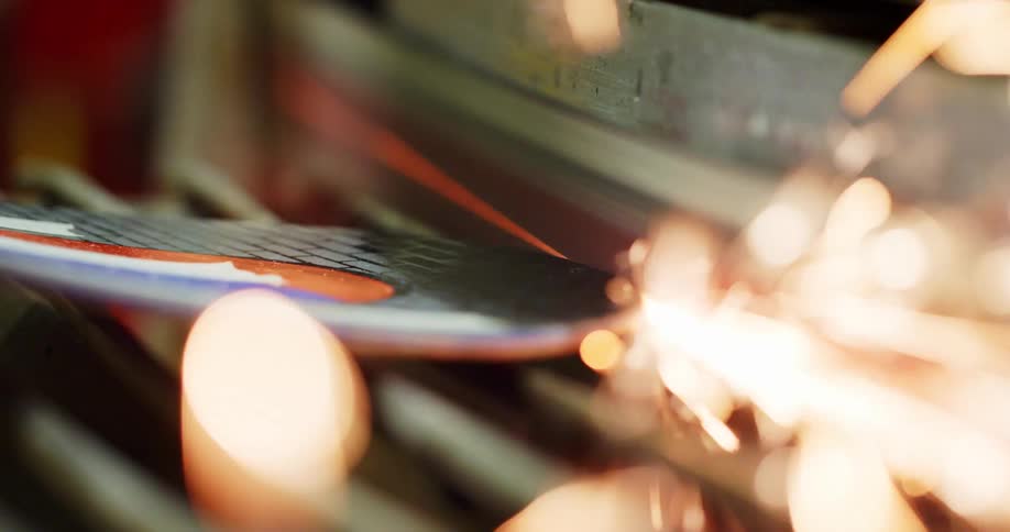 Large sparks fly as a round piece of metal is grinded by a machine