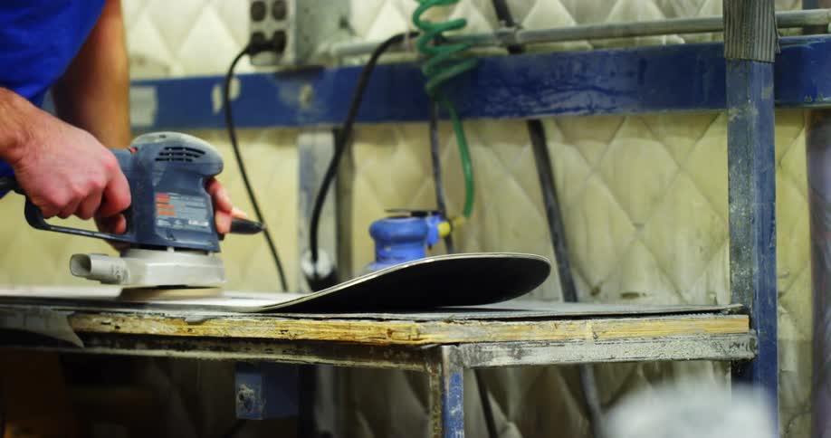 Man polishes board sitting on workbench with power tool