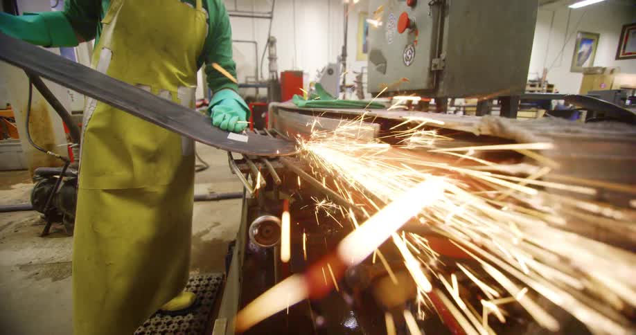 A man uses a metal grinder to smooth out a snowboard hes making