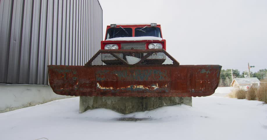 Snow plow sits in snow next to building