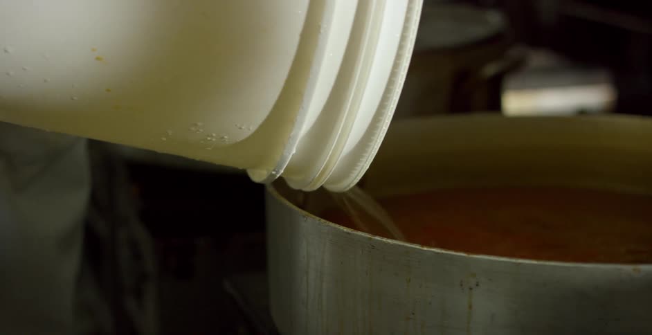 Person poursliquid from white bucket into large pot on stove