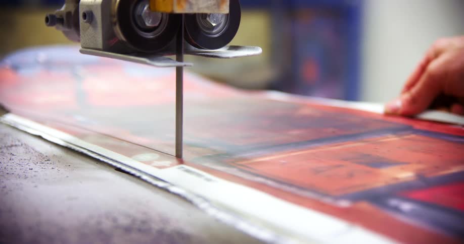 A person cutting out a snowboard with a saw in a factory