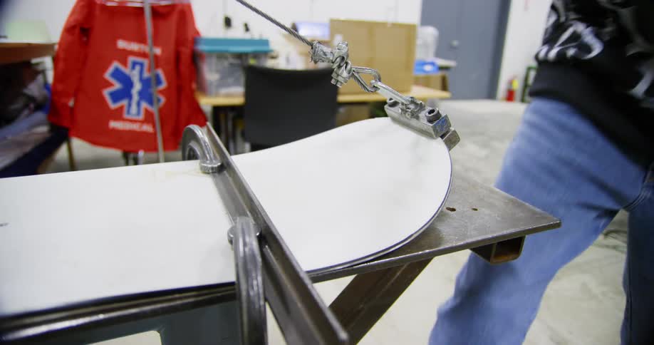 A man shapes a large piece of foam on a table using a wire cable cord