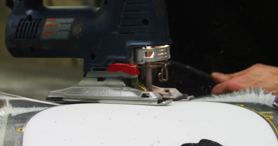 A man runs a sander along the edge of a large piece of plastic with a curved end