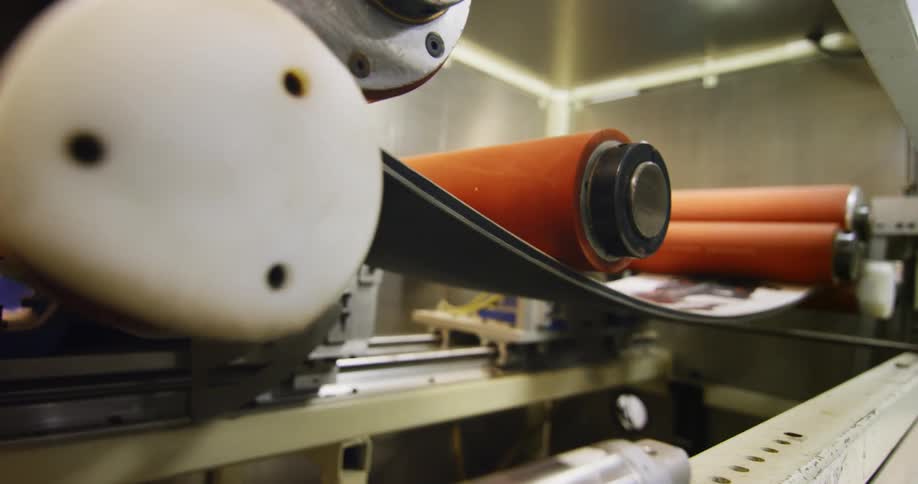 Automated machinery clamps down on and bends a plastic strip with an image on it