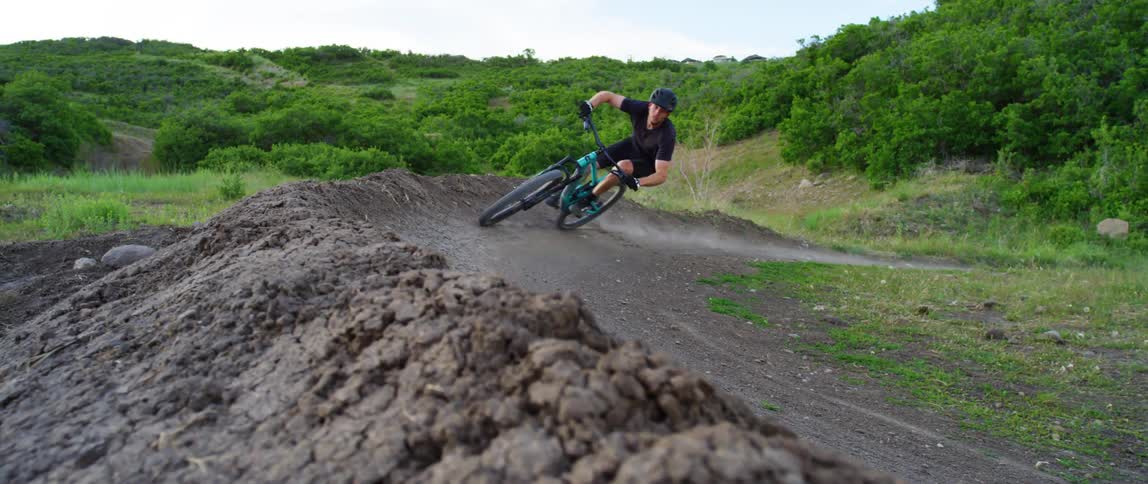 A man with a helmet and sunglasses riding a bike on a dirt road obstacle