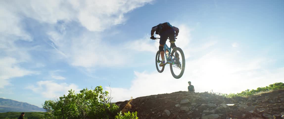 A biker jumping a dirt hill as a man watches