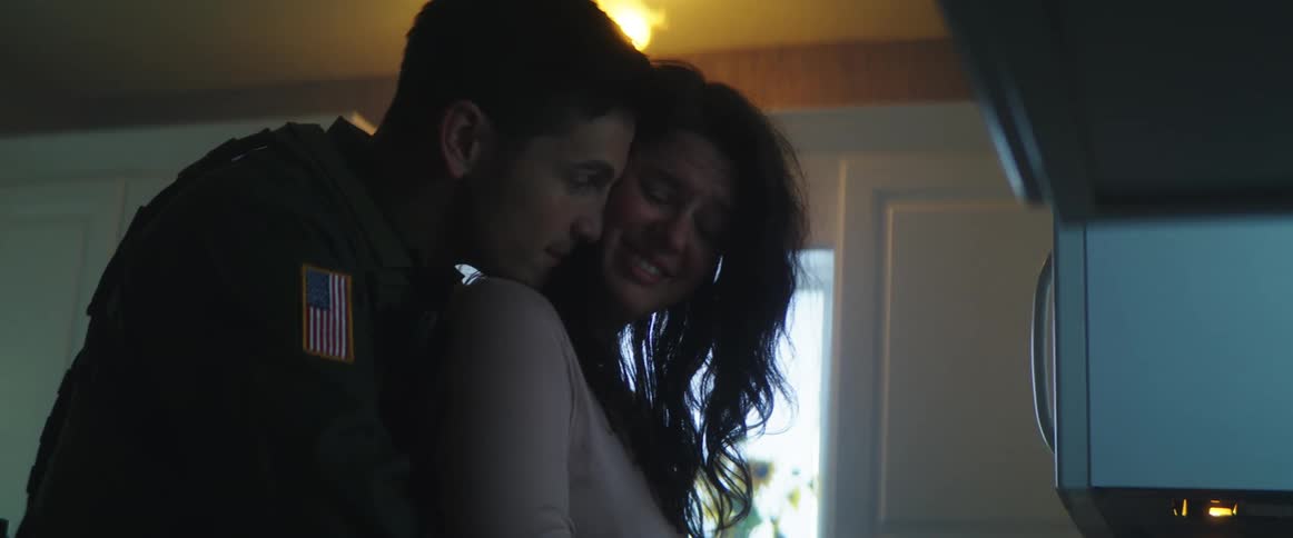 A man with a uniform hugging and talking to a woman in the kitchen