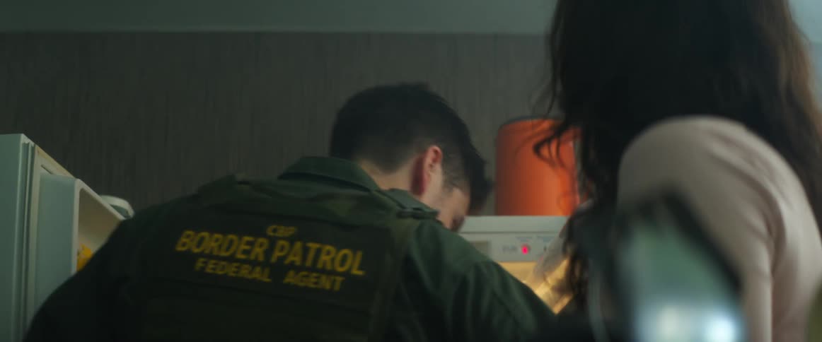 A border patrol agent in uniform opens his refrigerator and talks to his wife