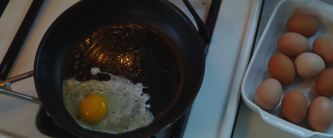 Womans hands crack an egg into a pan in the kitchen