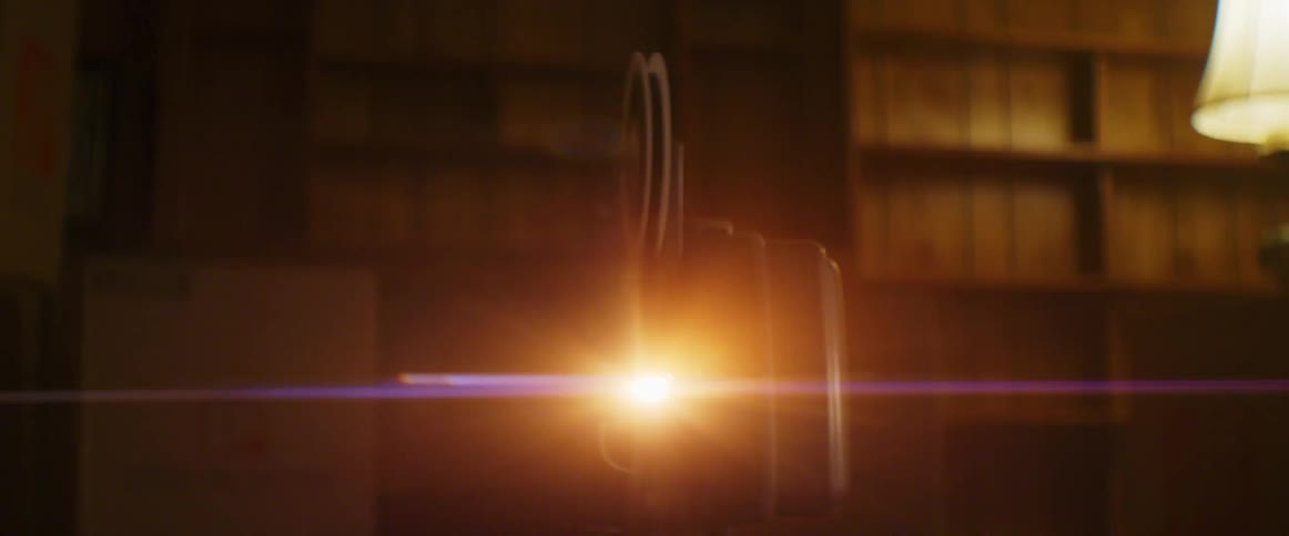 Light shines brightly on film projector in room lined by shelves