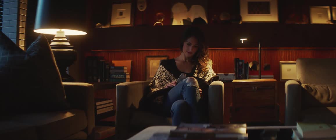 Woman with wavy hair and ripped jeans sits in an armchair and uses a tablet