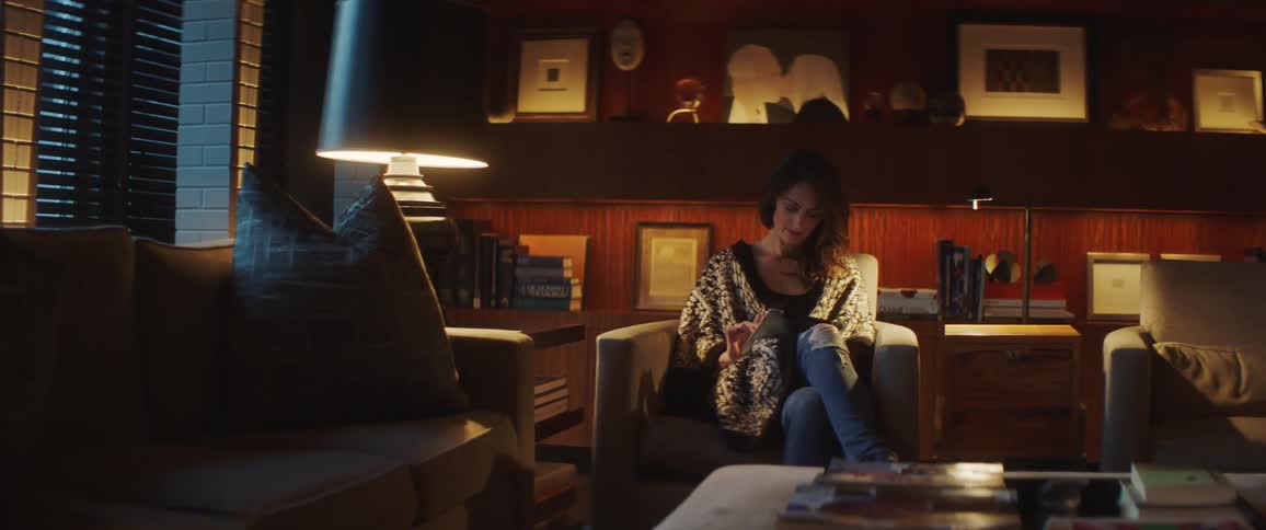 A woman uses a tablet while sitting in a chair in the living room of a house