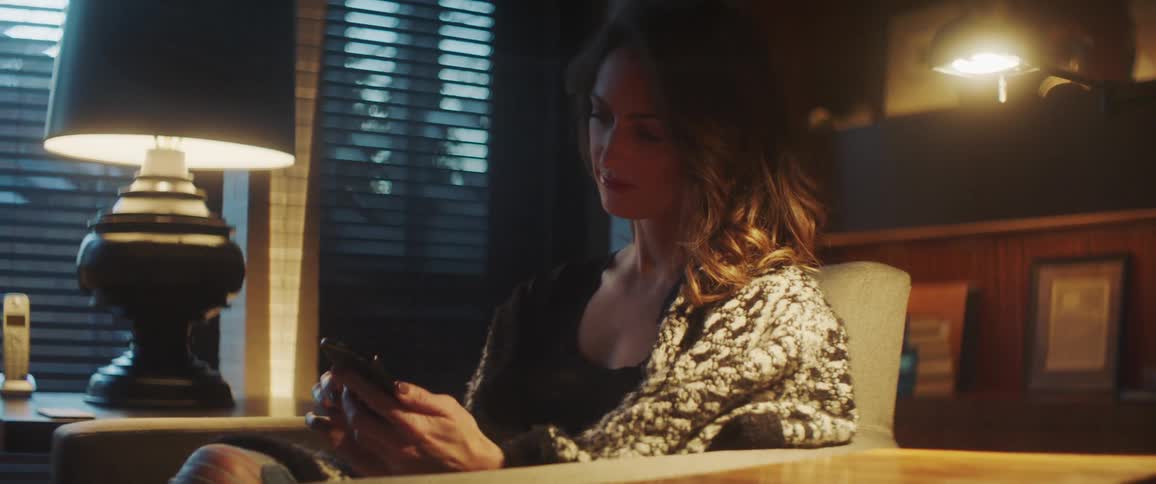 Woman with wavy hair sits in an armchair and uses a smartphone in a room
