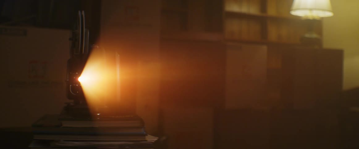 A projector on books projecting with shelves and a lamp in the background