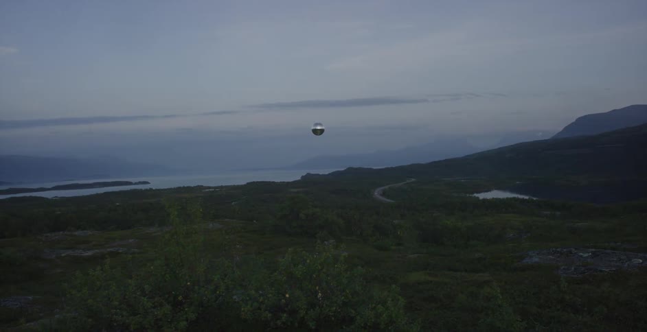 A silver glove is floating high above a green field