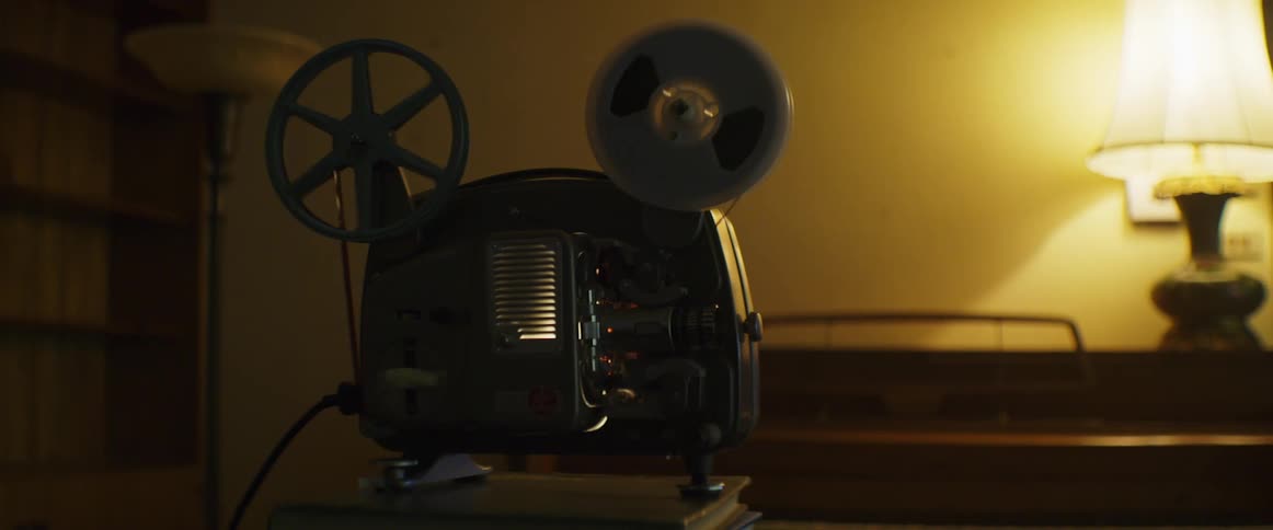 A projector on books with a bookshelf lamps and a wall in the background