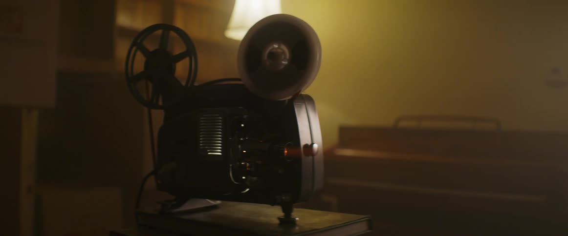 The reels of a small film projector spin as it projects an image out of frame