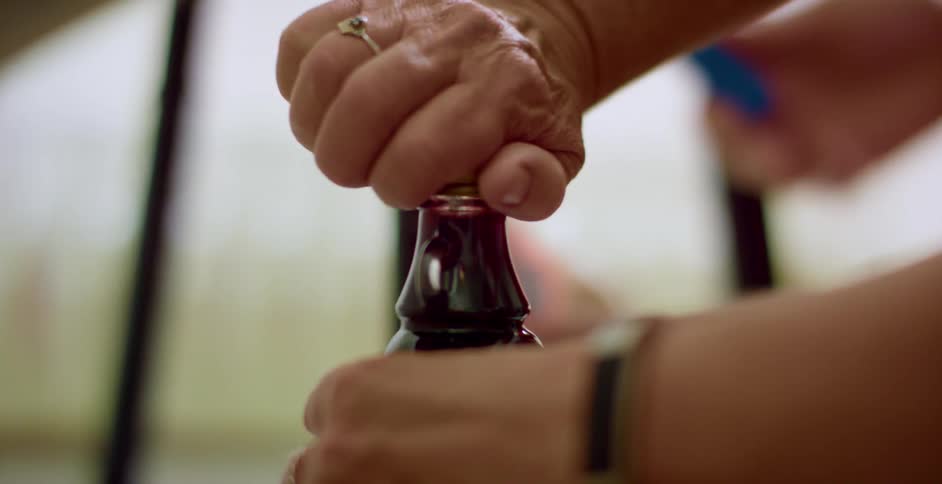 A person putting on a cap on a bottle with another person with a smart phone in the background