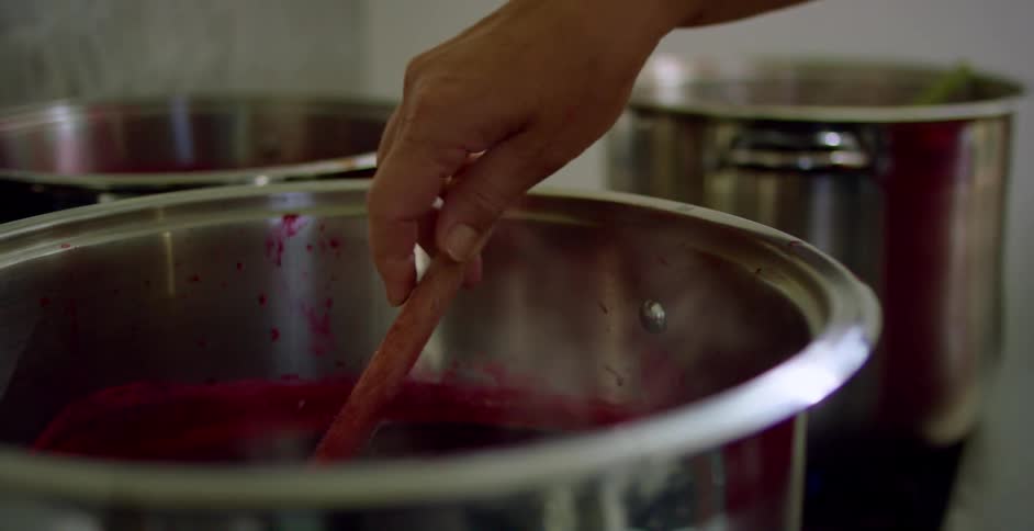 Person stirs pot of red sauce steaming on the stove