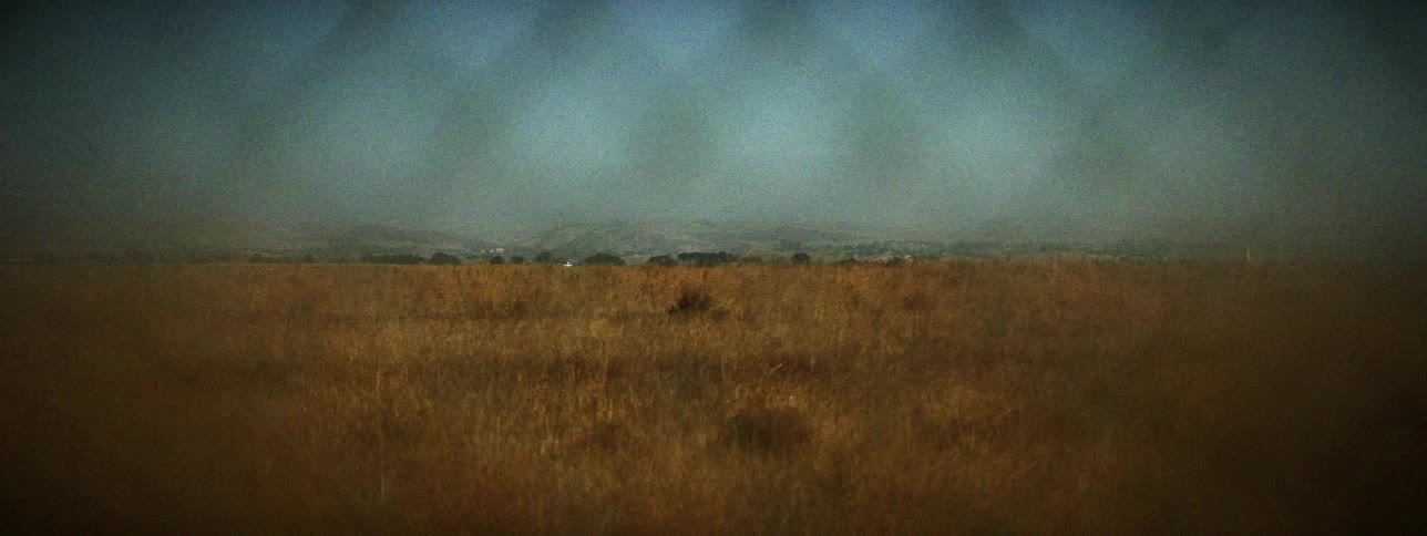 A large field and mountain range are visible in the distance through a chain link fence
