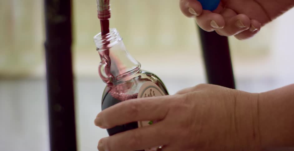 A man fills a small glass bottle with dark red liquor