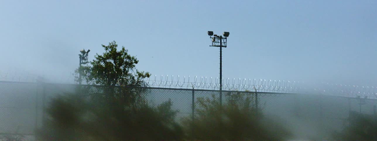 A tall fence with barbed wire lining the top under a clear sky during the day