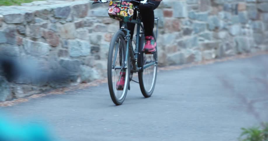 Woman with black pants and pink shoes rides a bicycle on a road