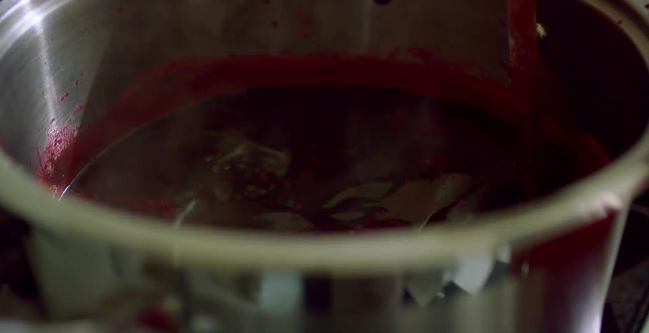 A person stirs a pot of cooking food with a wood spoon