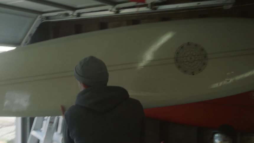 A man grabs a surfboard and carries it over to a vehicle