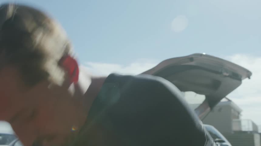 A man is putting on a wetsuit in a lot