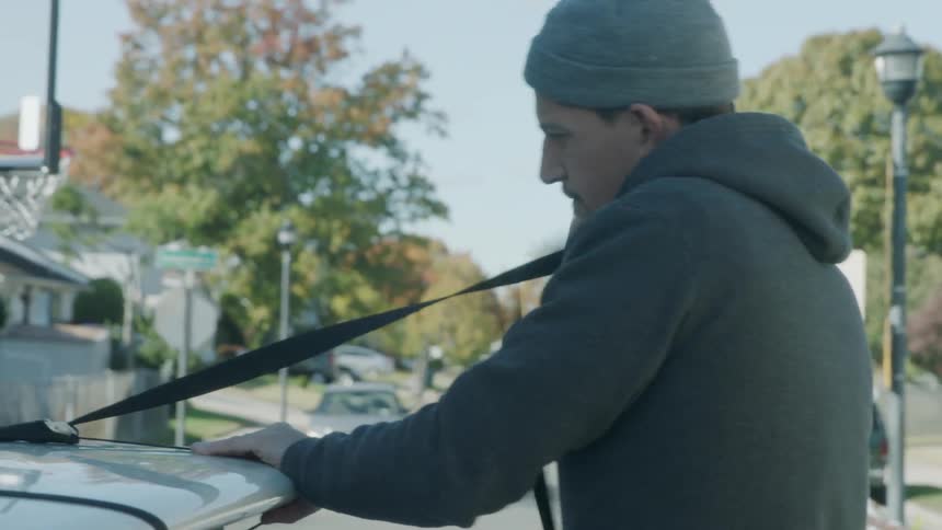 A man is attaching a surfboard to the top of his car