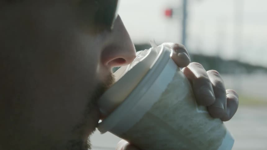 A man drinks from a cup in a vehicle