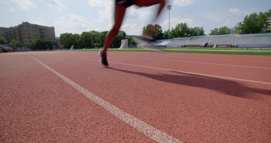 A young woman sprints along the center lane of a running track on a sunny day