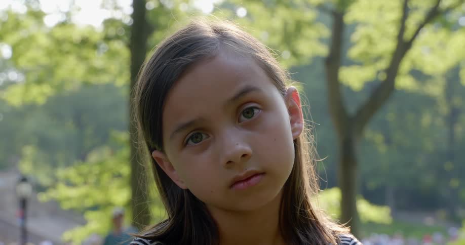 Girl with a long brown hair faces the camera with eye contact in park