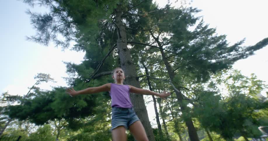 A girl adjusts the camera before performing dance moves in front of a tall tree on a sunny day