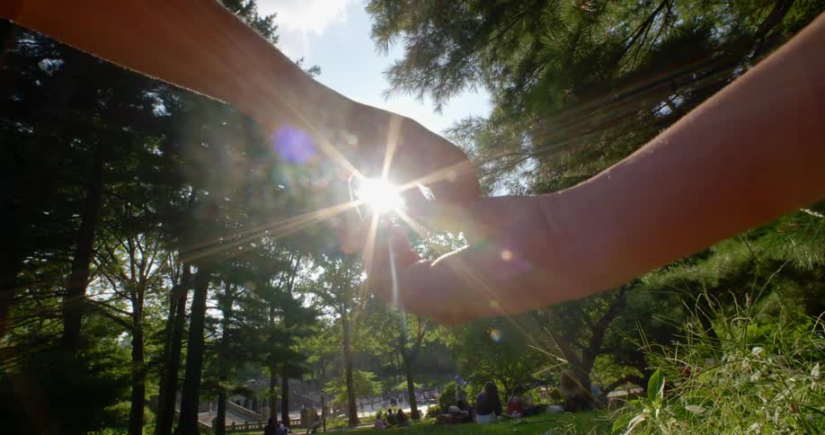Two hands slowly closing into each other with sunlight filtering through on a park