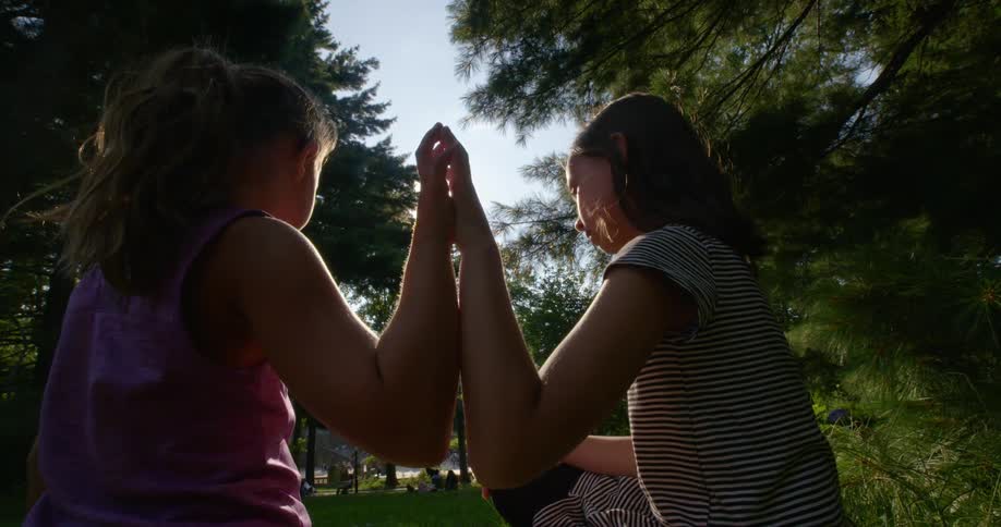Girls sitting in the grass on a park hold hands at sunset