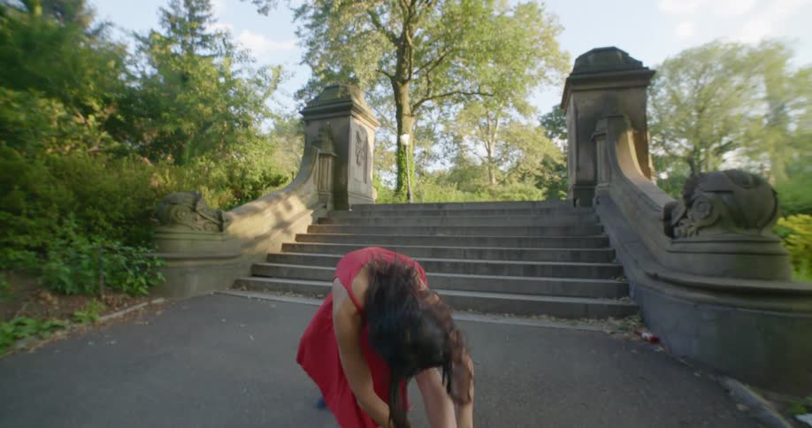 Woman wearing red dress dances near steps in park